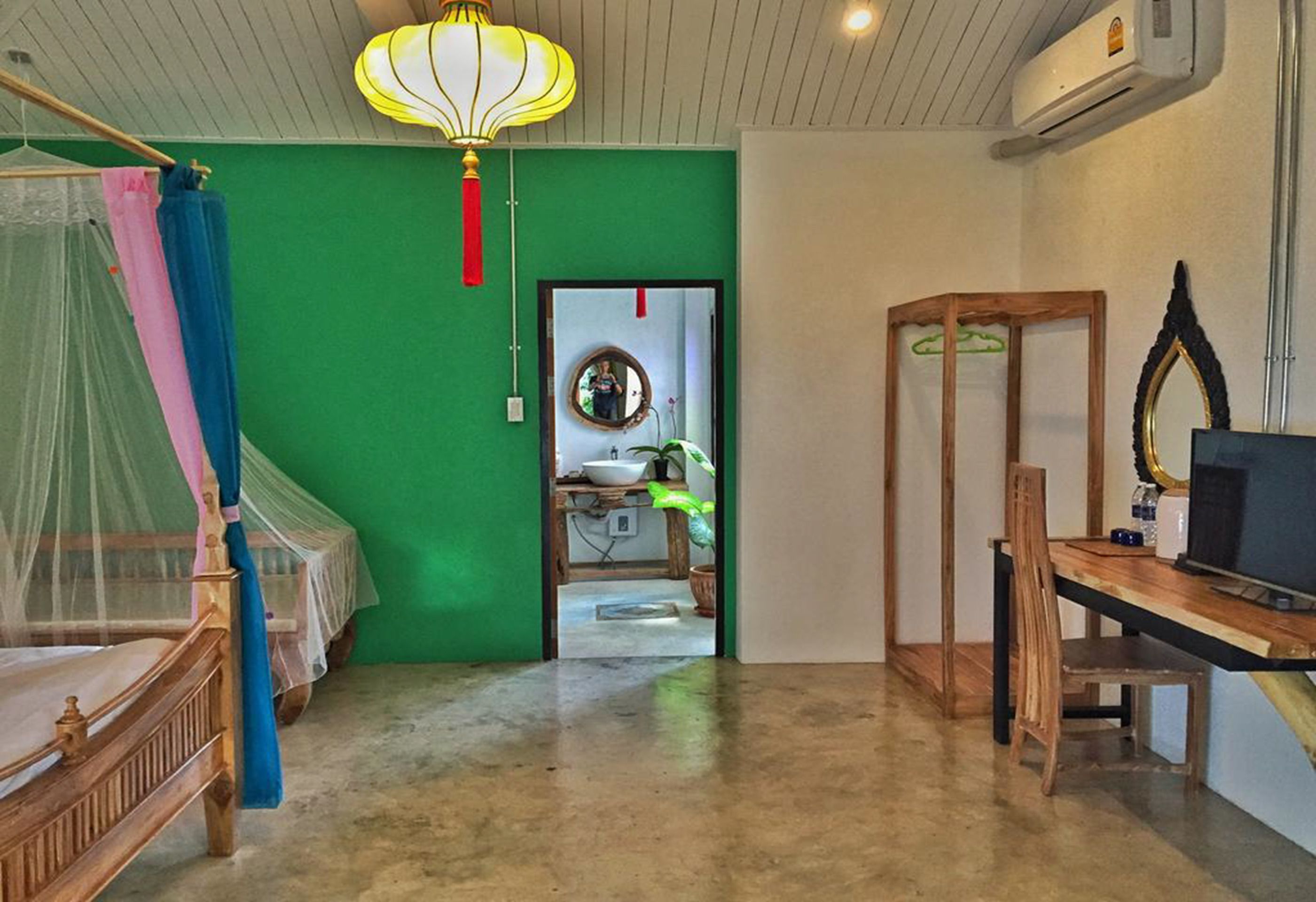 A room with a bed, a desk, a chair, a television, and a green wall.
