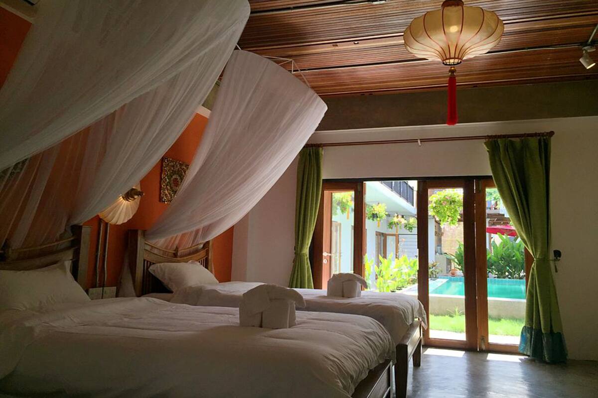A room with two beds, a canopy, a hanging lantern, and a view of a pool.