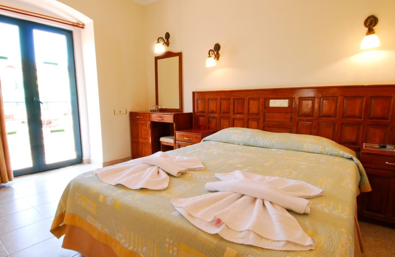 A hotel room with a large bed, wooden headboard, a dresser, and a mirror.