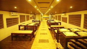 A hotel corridor with rows of tables and benches, air conditioning units on the walls, and a central carpeted walkway.