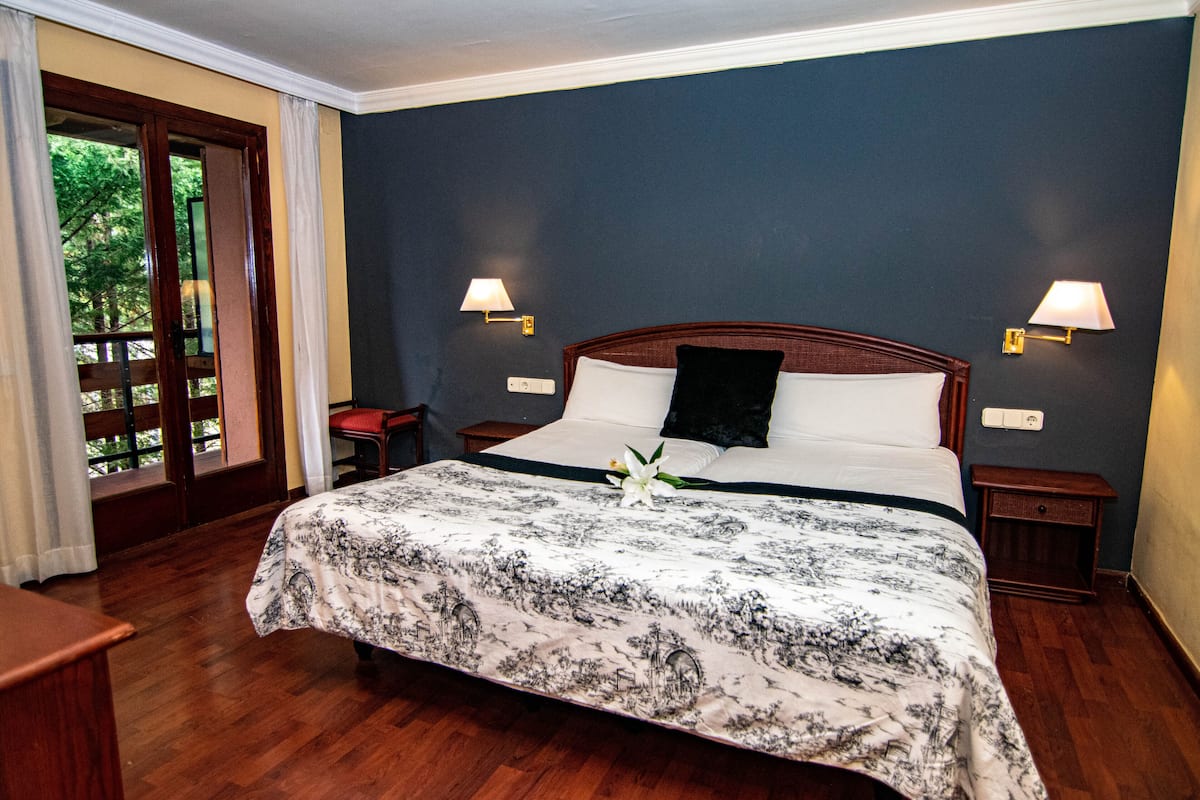 A hotel room with a large bed, two bedside lamps, a nightstand, and a view of the outdoors through a glass door.