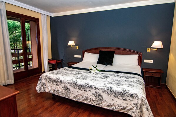 A hotel room with a large bed, two bedside lamps, a nightstand, and a view of the outdoors through a glass door. - Hotel Moixeró (Prats i Sansor)