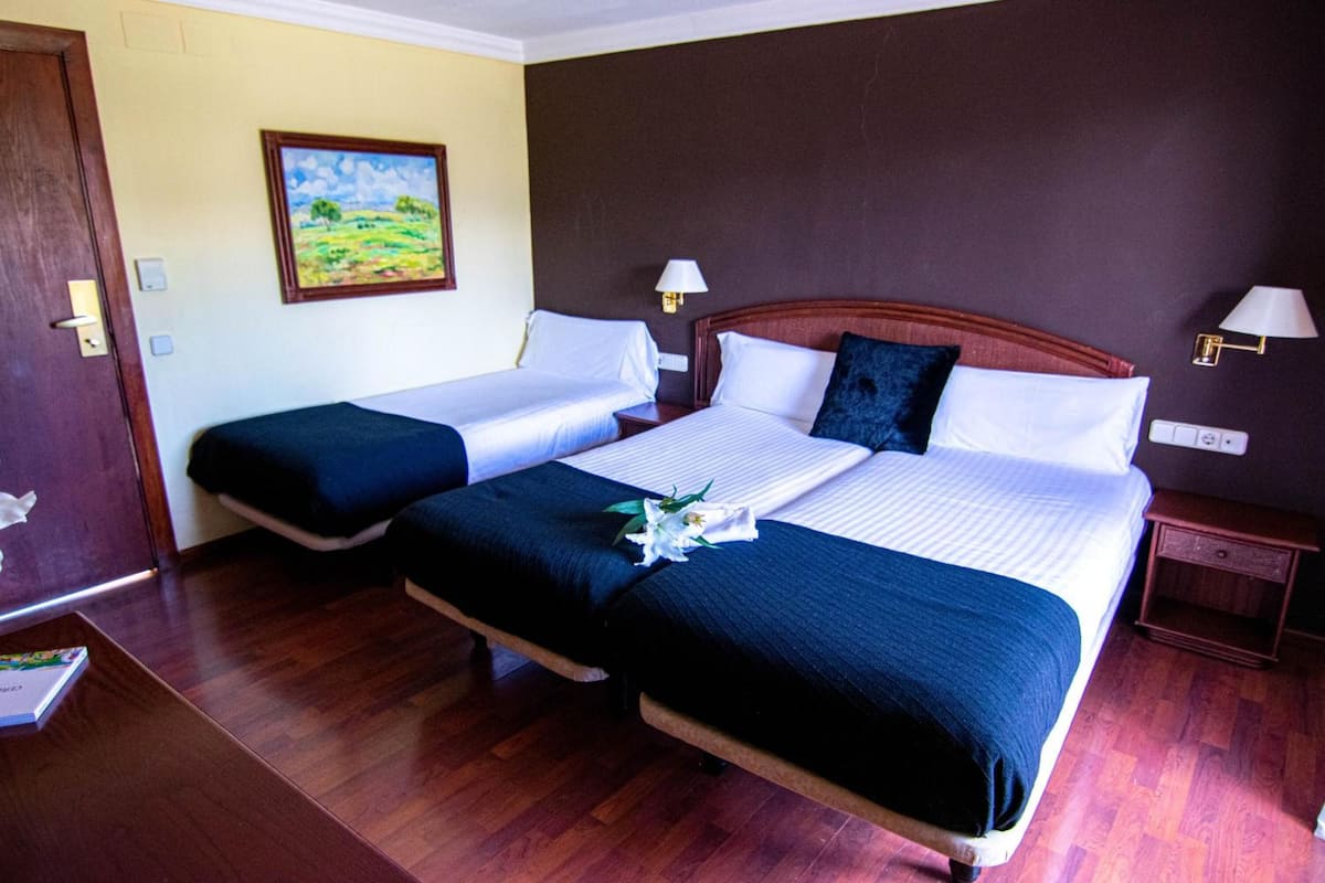 A hotel room with two beds, wooden flooring, a painting on the wall, and bedside lamps.