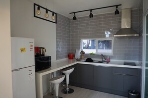 A modern kitchen with grey tiled backsplash, a stainless steel range hood, a microwave, a sink, and a window with a view of trees.