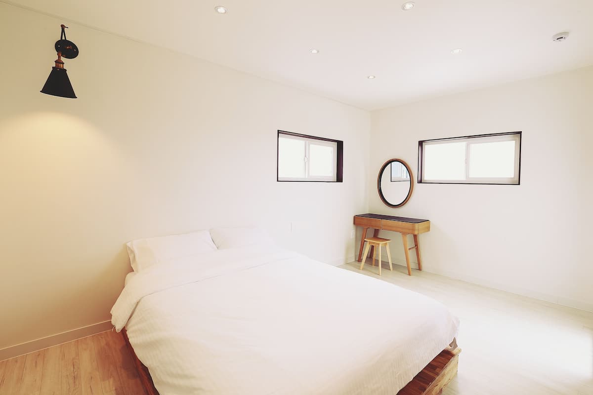 Un dormitorio con cama, escritorio y dos ventanas.