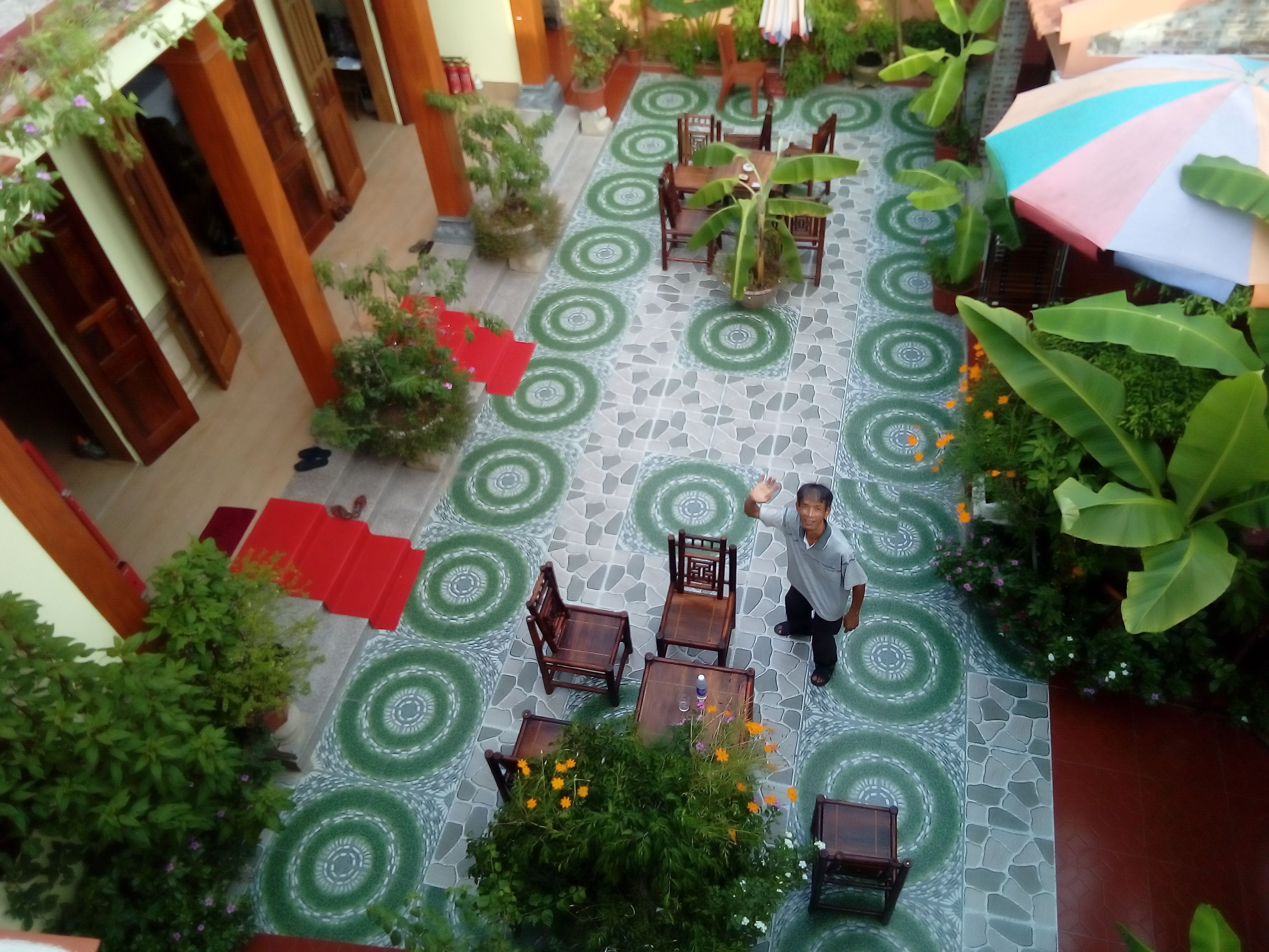 Un patio exterior con suelo de baldosas, mobiliario de madera y plantas en macetas.