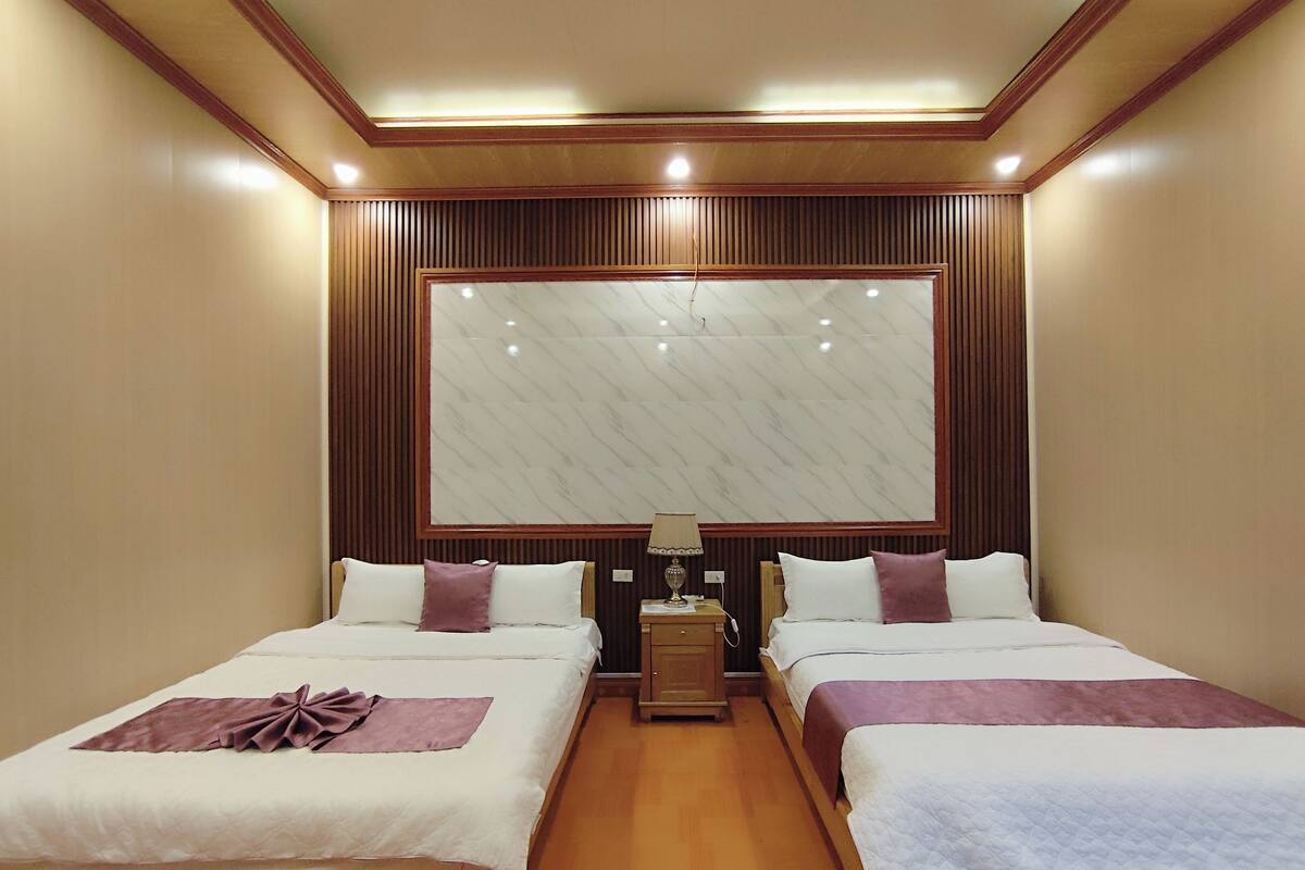 A hotel room with two beds, wooden paneling, a large mirror, and a nightstand with a lamp.