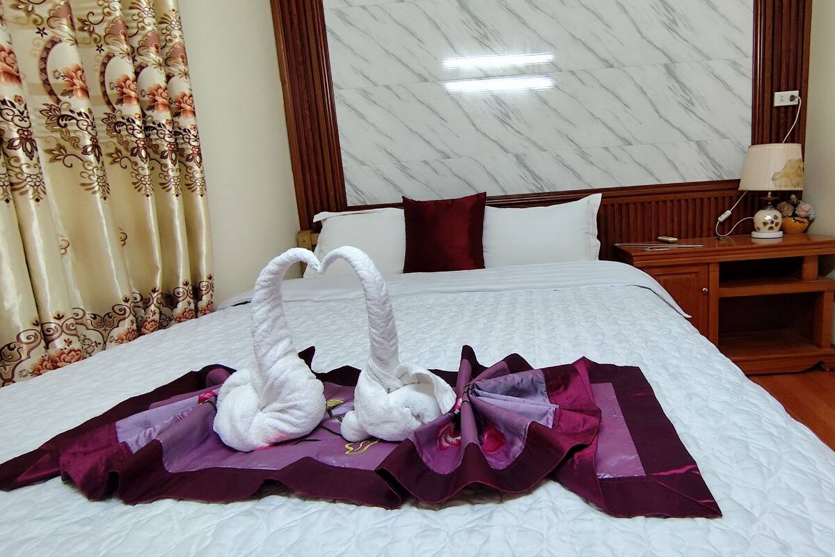 A hotel room with a neatly made bed, a wooden nightstand with a lamp, and a marble-patterned wall.