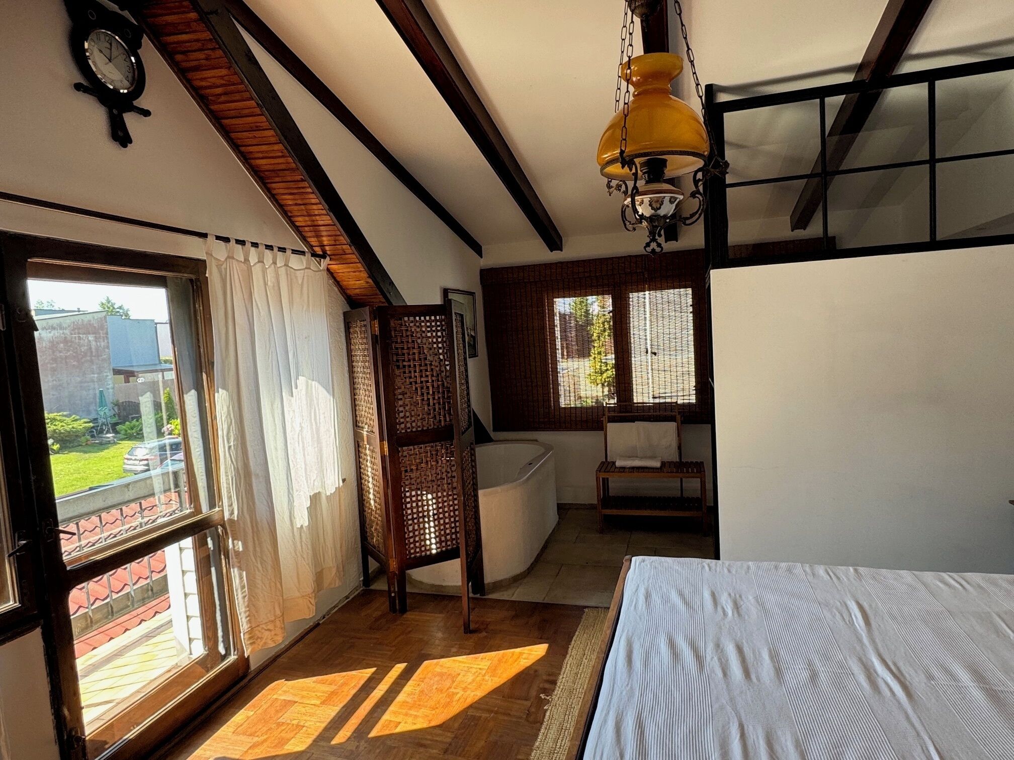 Une pièce avec un lit, une fenêtre avec des rideaux, un plancher en bois, un luminaire suspendu et une vue sur l’extérieur.