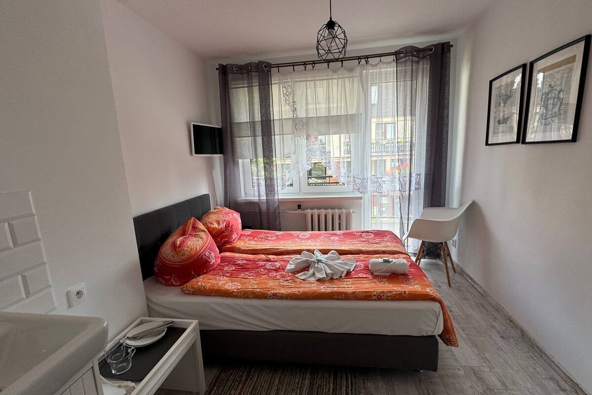 Quarto de hotel com duas camas, uma escrivaninha, uma cadeira, uma televisão e uma janela com cortinas.