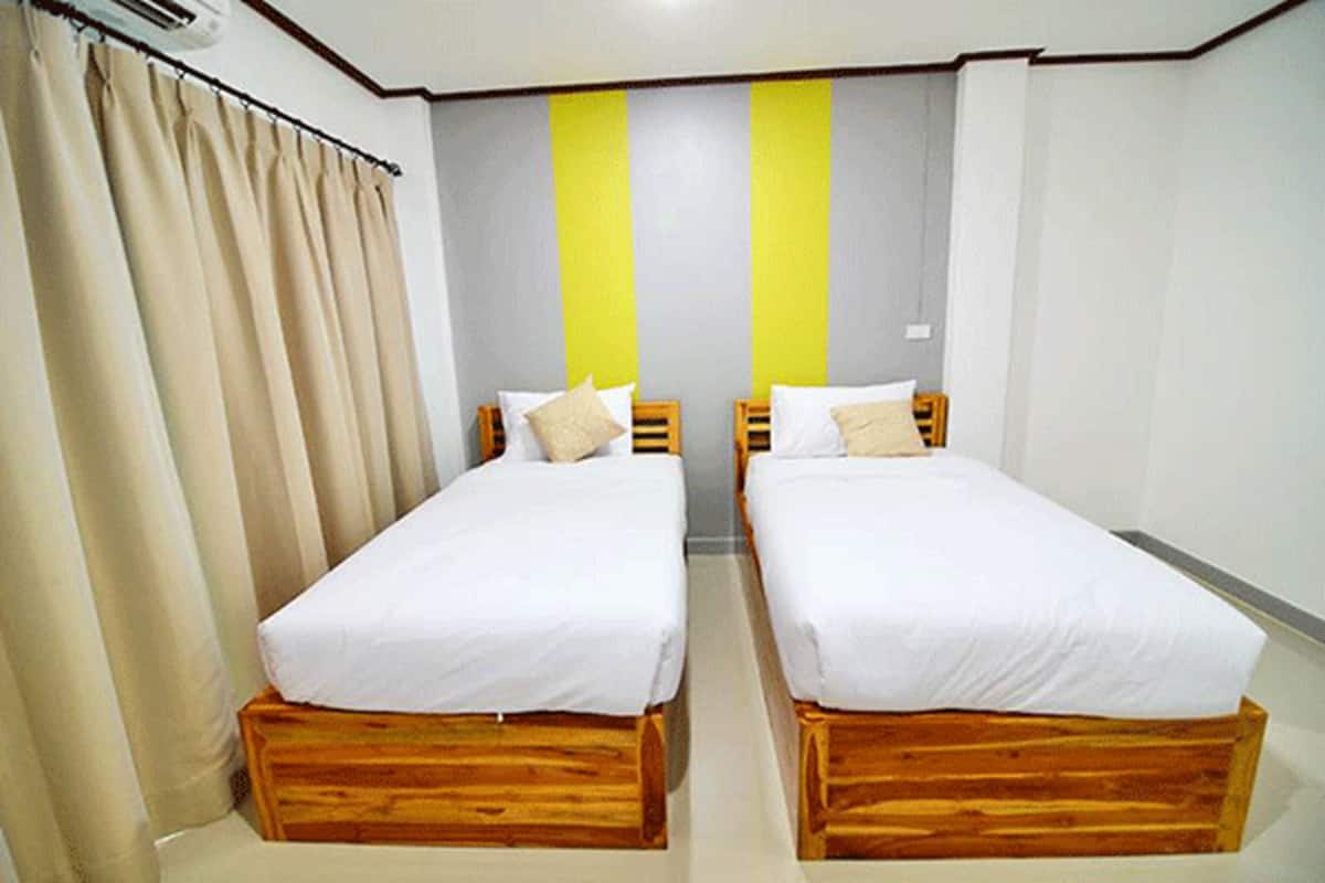 Quarto com duas camas de madeira, cortinas bege e parede listrada em amarelo e cinza.