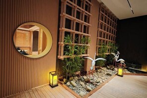 Un intérieur de style japonais traditionnel, avec un mur en bois, un miroir rond et une petite fontaine ornée d’oiseaux décoratifs.