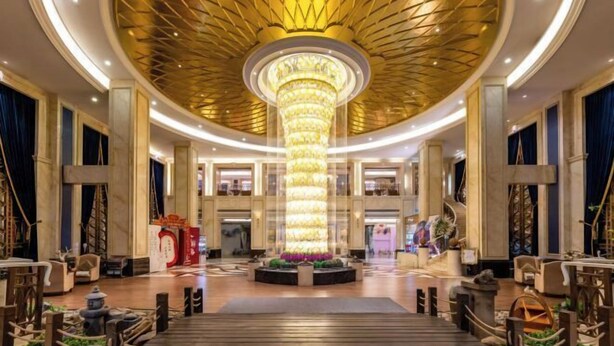 A grand lobby with a central chandelier, a circular seating area, and a staircase leading to upper floors.