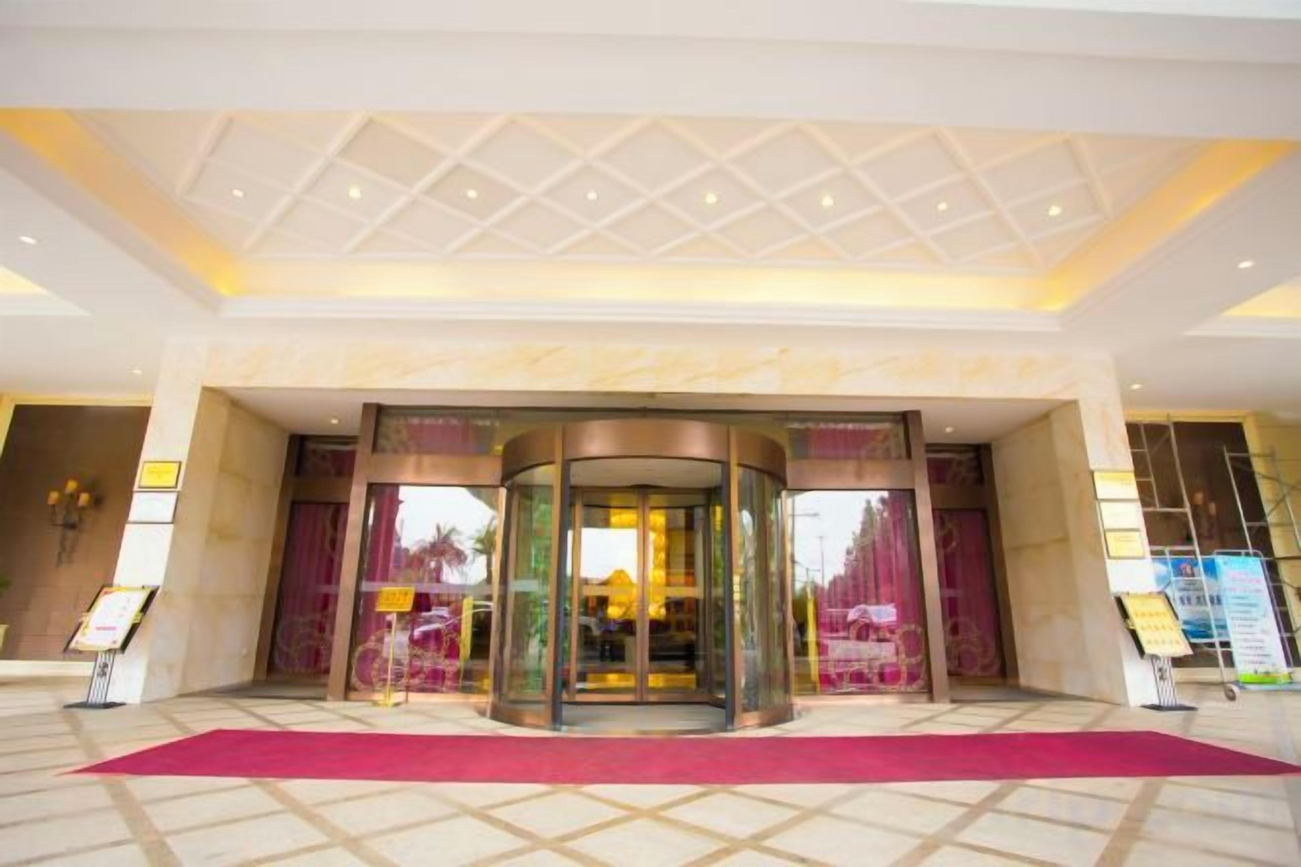 Un vestíbulo de hotel con puerta giratoria, alfombra roja y suelo de baldosas.