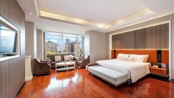 A modern hotel room with a large bed, a sofa, a coffee table, and a TV.