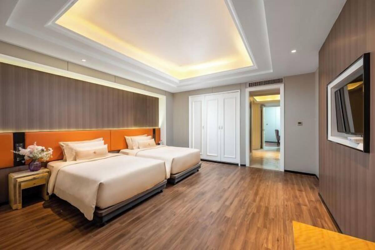 Une chambre d’hôtel moderne avec deux lits, un plancher en bois, une grande fenêtre et un téléviseur fixé au mur.