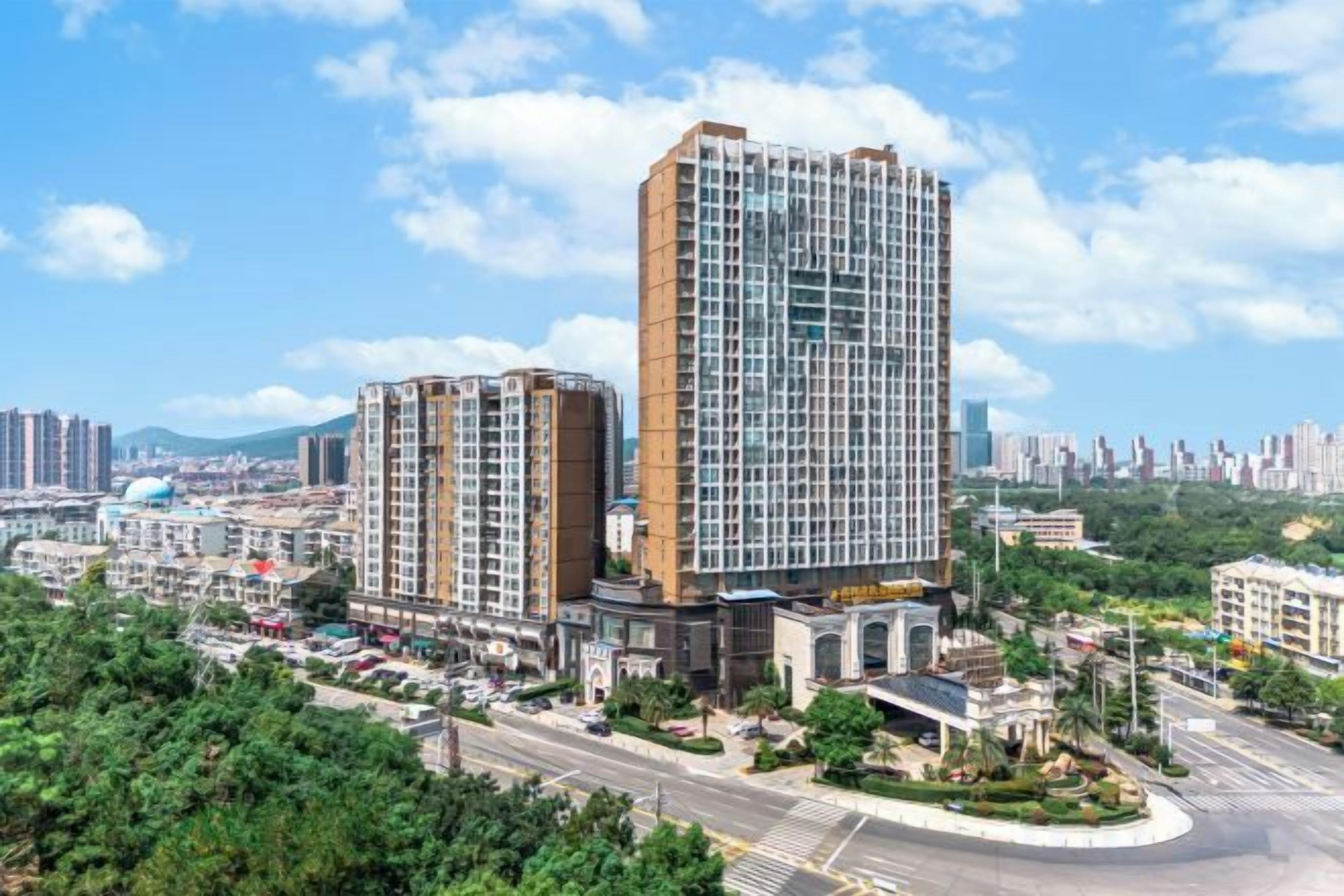 A high-rise hotel with multiple floors, surrounded by greenery and a clear sky.
