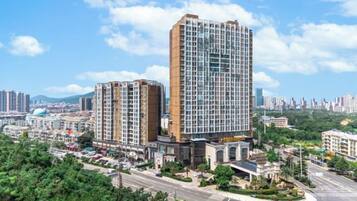 A high-rise hotel with multiple floors, surrounded by greenery and a clear sky.