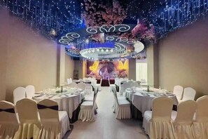 Une salle de banquet avec des tables rondes, des chaises blanches et un plafond décoratif.