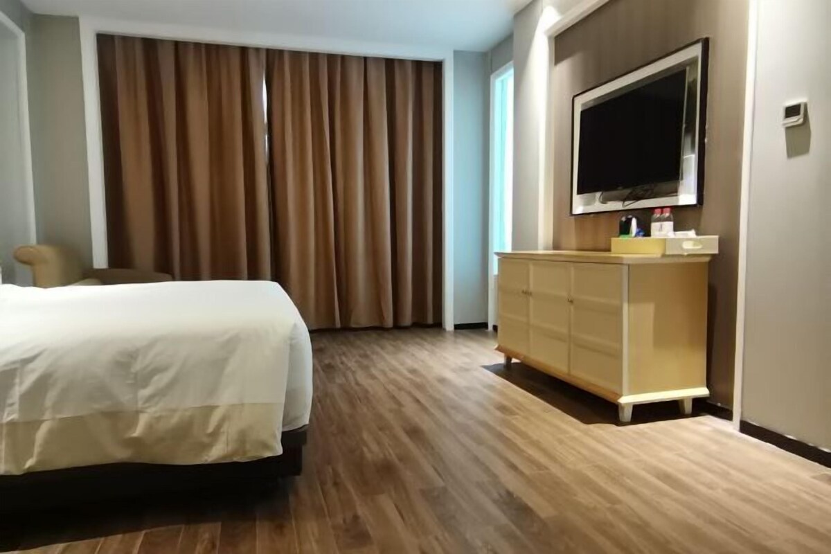 Hotelkamer met een bed, een aan de muur bevestigde televisie, een houten vloer en een raam met gordijnen.