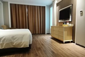 Hotelkamer met een bed, een aan de muur bevestigde televisie, een houten vloer en een raam met gordijnen.