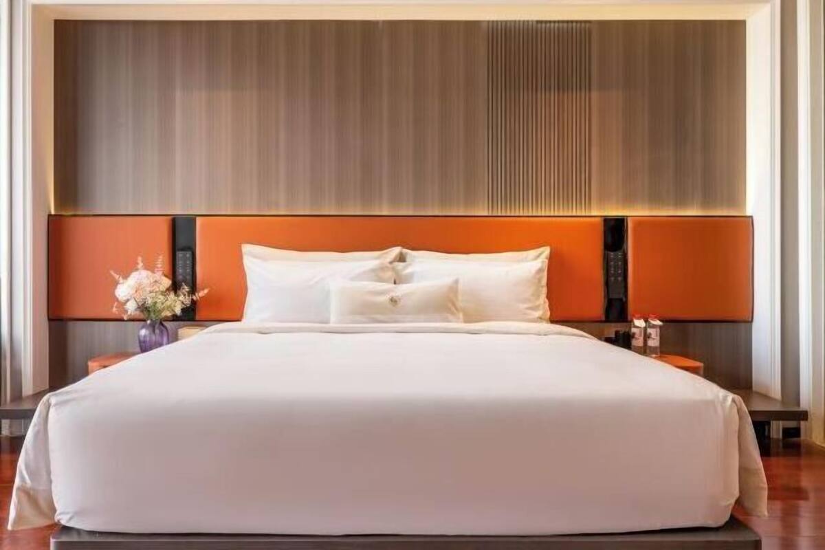 Une chambre d’hôtel moderne avec un grand lit, une tête de lit en bois et une table de chevet agrémentée d’un vase de fleurs.