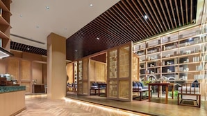 A modern interior with a wooden reception desk, seating area, and a bookshelf filled with books.