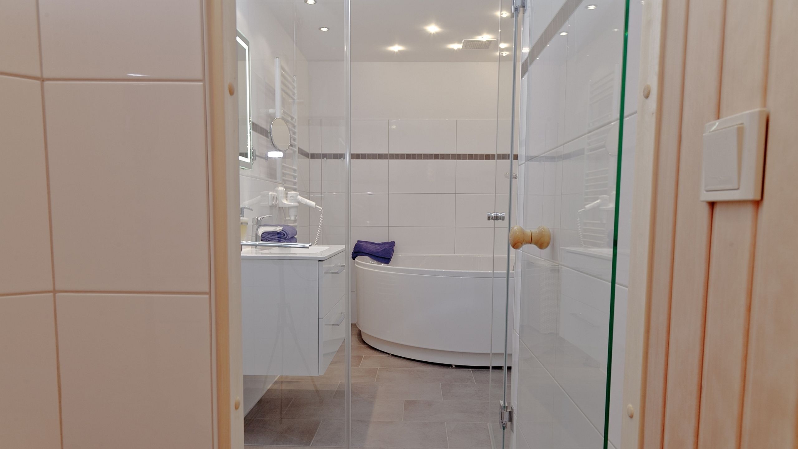 A modern bathroom with a glass shower enclosure, a white bathtub, and a vanity with a mirror.