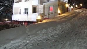 Un edificio de varios pisos con balcones, suelo cubierto de nieve y una valla.
