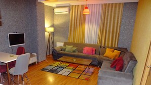Una sala de estar moderna con un sofá gris, una mesita, un sillón rojo, un televisor y una lámpara de pie.