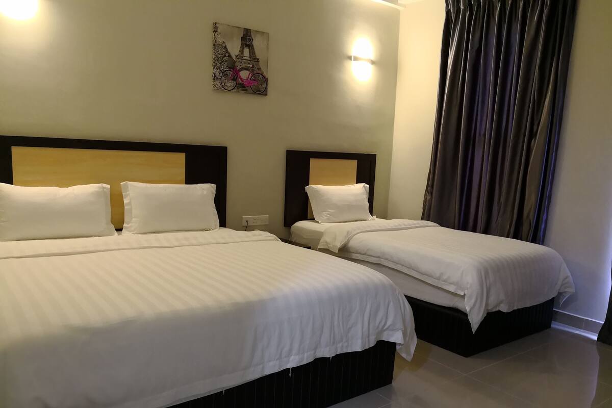 A hotel room with two beds, a headboard with a light fixture, a wall-mounted artwork, and a window with curtains.