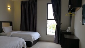 Ett hotellrum med två sängar, ett fönster med gardiner, ett nattduksbord med en vattenkokare och en väggmonterad TV.