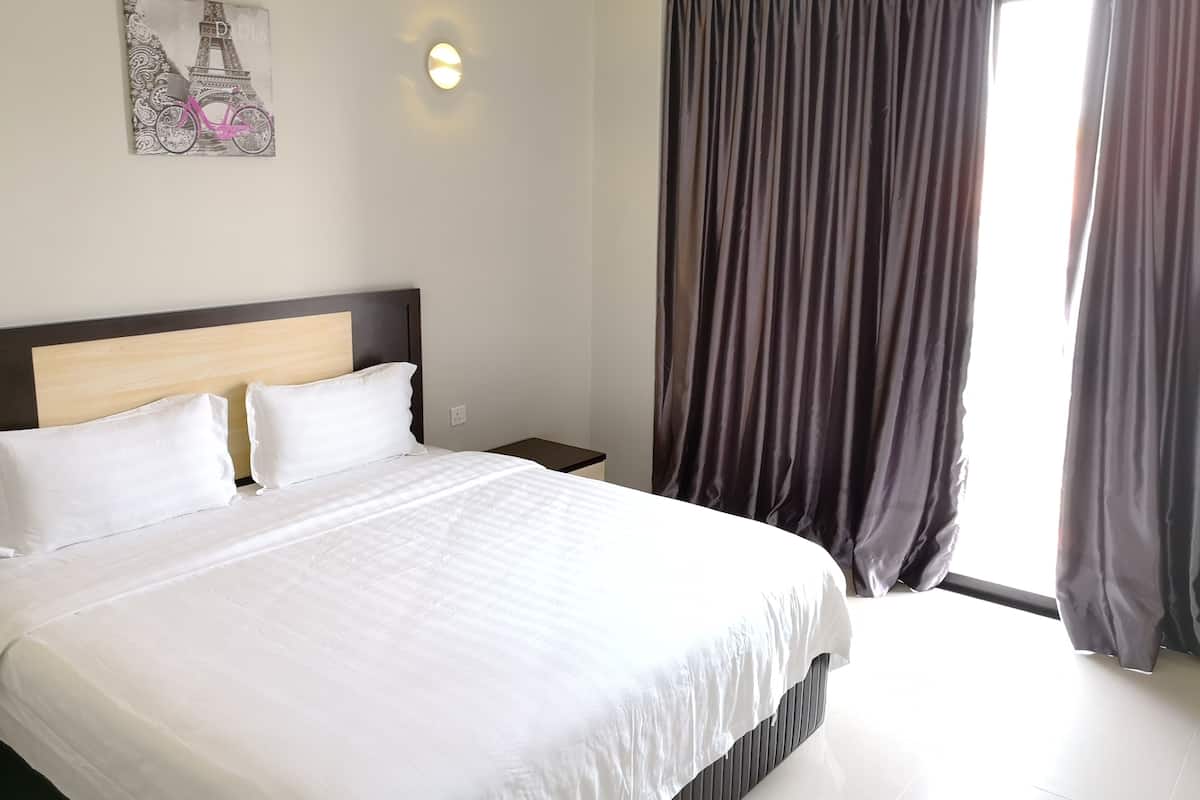 A hotel room with a large bed, a headboard, a nightstand, a wall-mounted light, and a window with curtains.