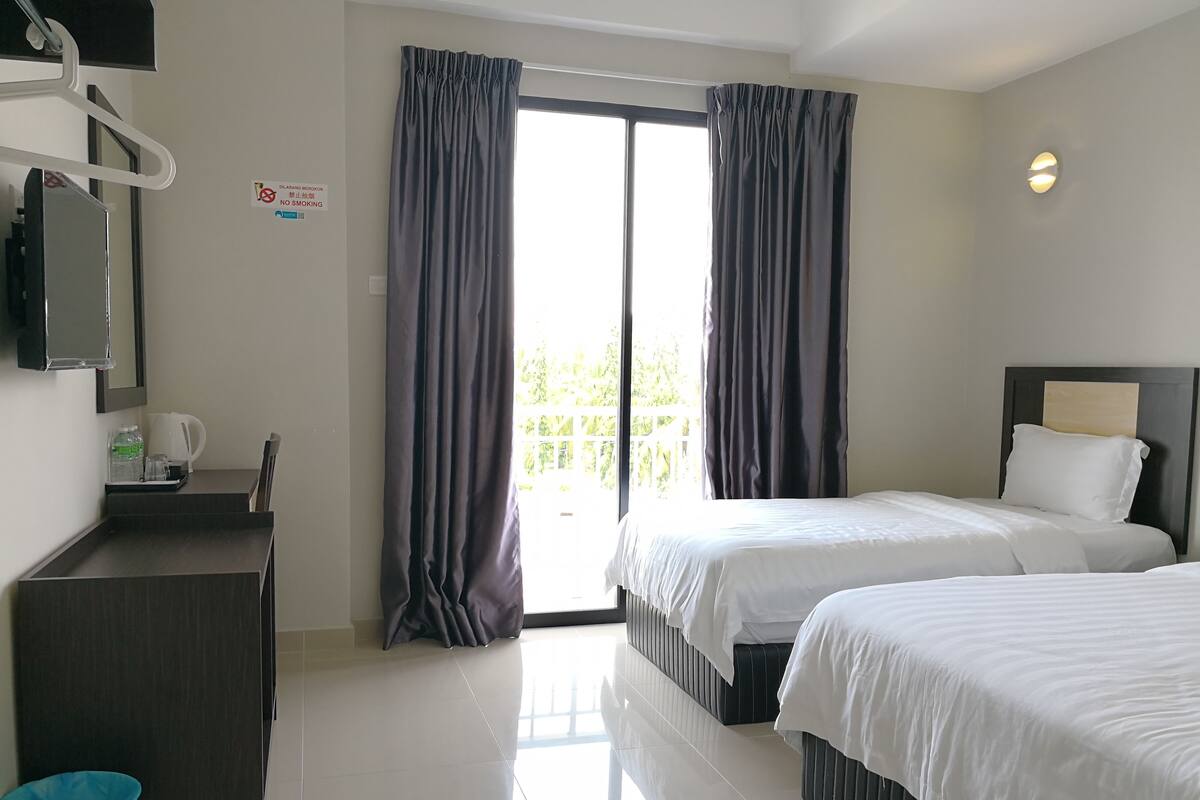 A hotel room with two beds, a desk with a chair, a TV, and a window with curtains.