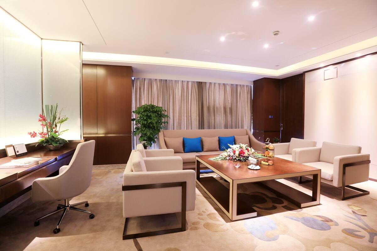 Une chambre d’hôtel moderne, dotée d’un canapé, d’un bureau avec une chaise, d’une table basse et d’une grande fenêtre avec des rideaux.