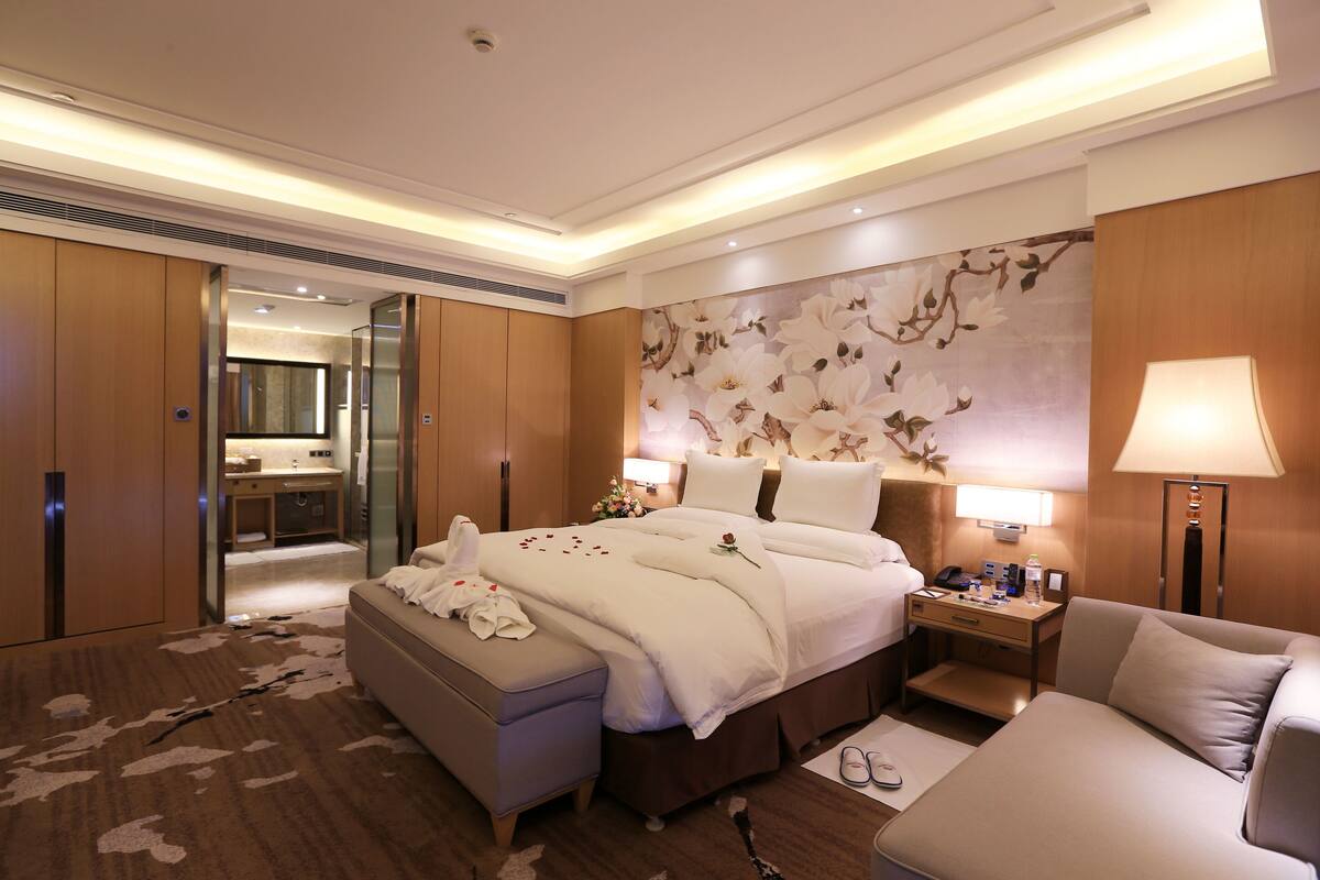 Une chambre d’hôtel avec un grand lit, un coin salon, un bureau et une salle de bain visible à travers une porte ouverte.