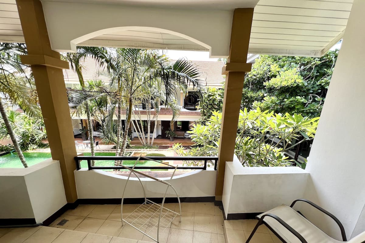 A balcony with a view of a courtyard, a metal rack, and a chair.