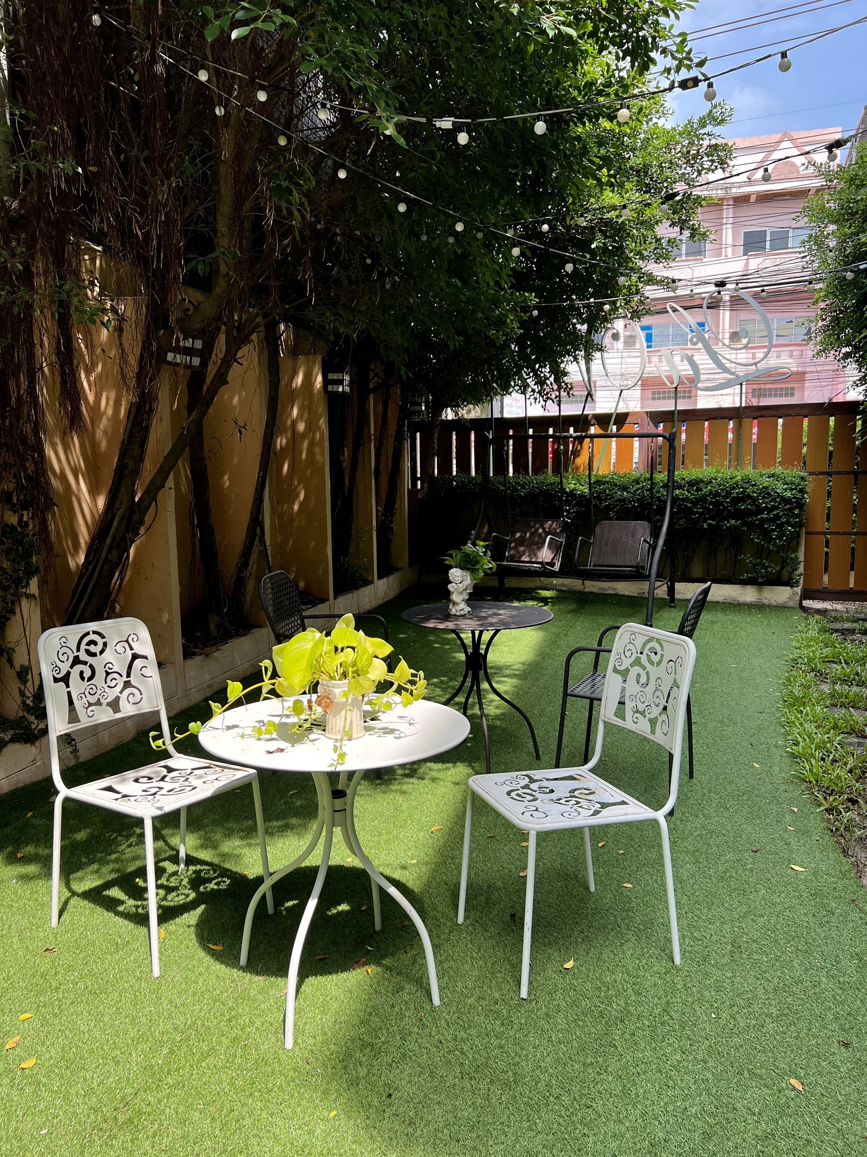 Un patio con erba sintetica, sedie in metallo bianco e un tavolo rotondo con un vaso di fiori.