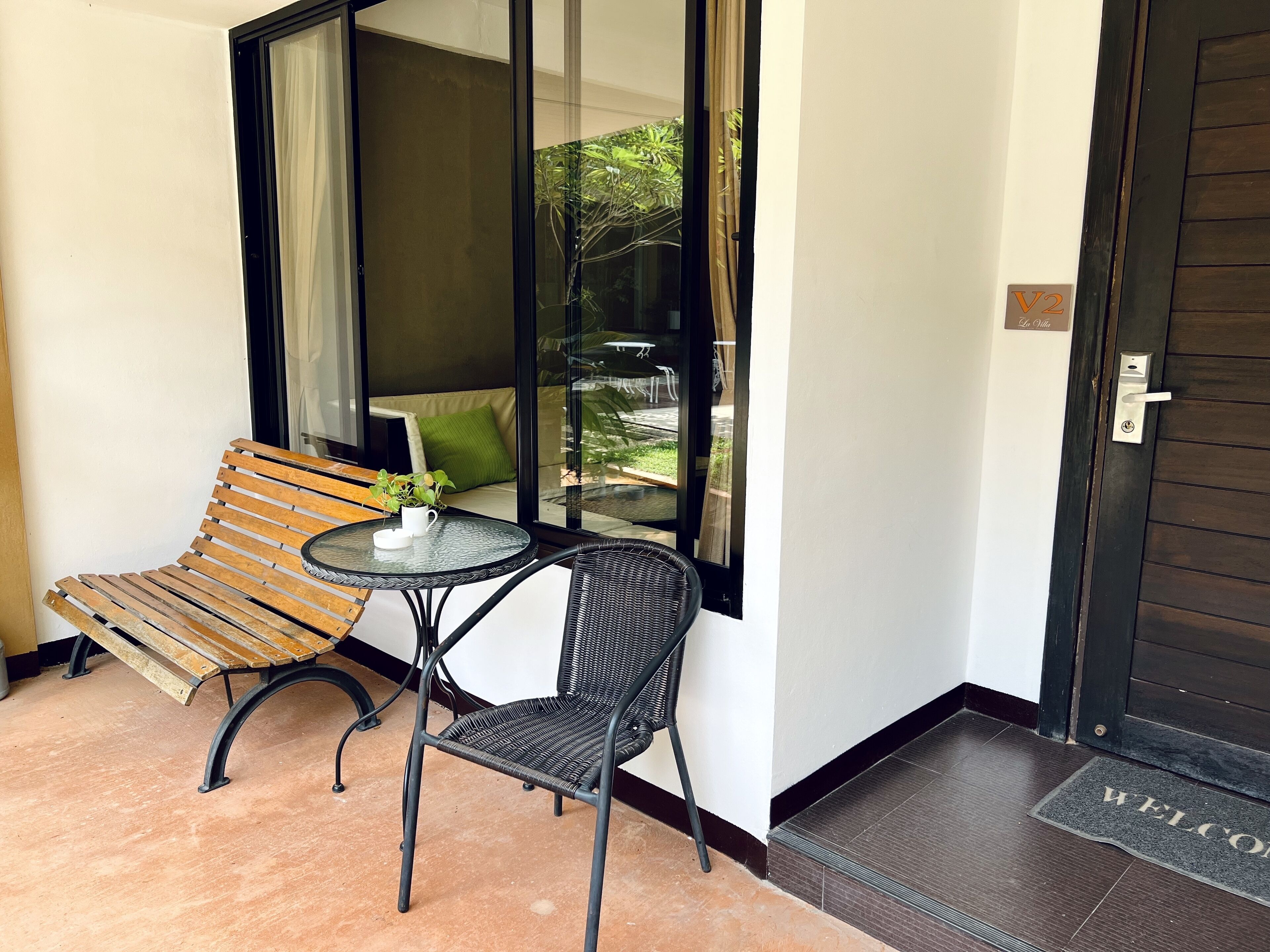 A balcony with a wooden bench, a wicker chair, and a small table with a plant.