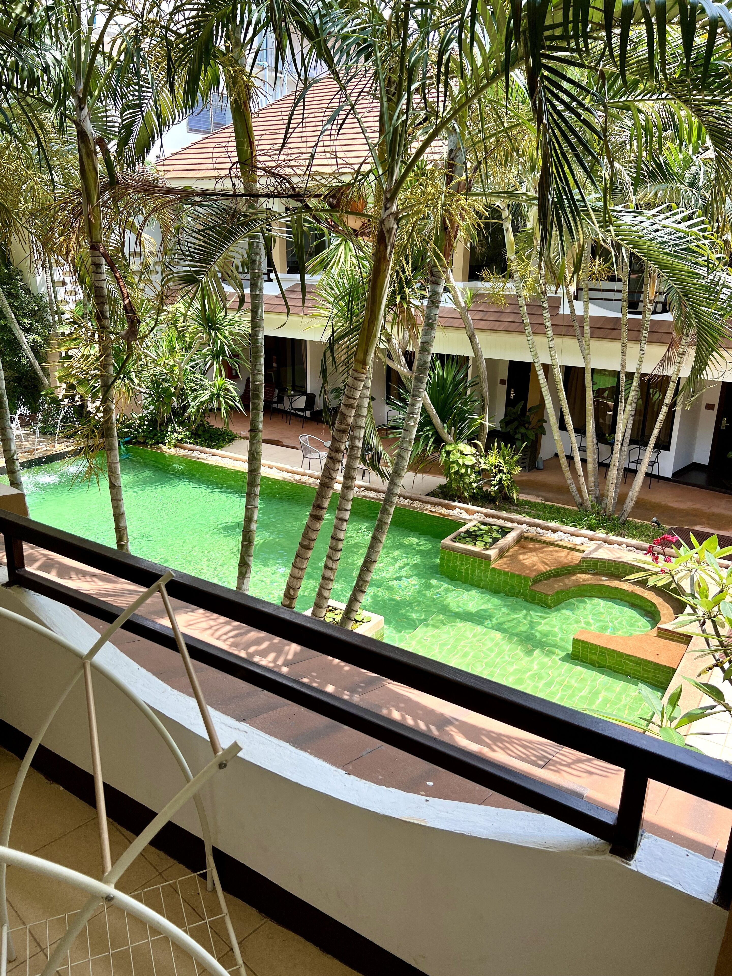 Un espace piscine agrémenté de palmiers, un coin salon abrité et un bâtiment doté d’un toit en tuiles.