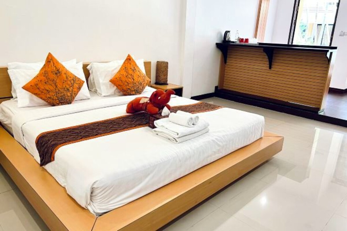A modern hotel room with a large bed, two pillows, a red plush toy, and a neatly folded towel.