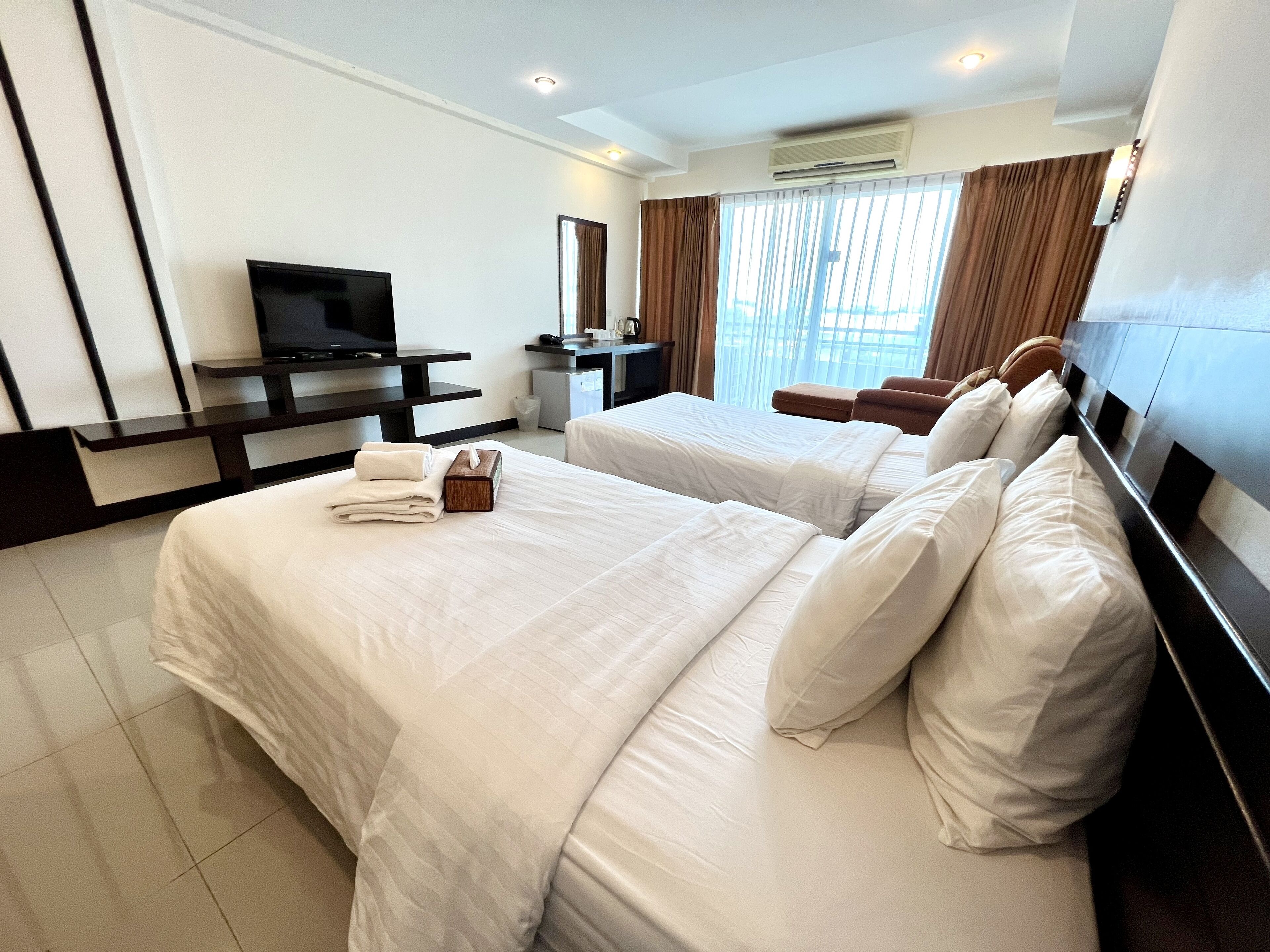 A hotel room with two beds, a TV, a desk, and a window with curtains.