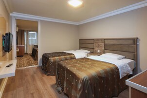 Habitación de hotel con dos camas, televisión, escritorio y baño visible a través de una puerta abierta.