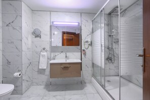 A modern bathroom with a marble floor, a sink with a mirror above it, a toilet, and a glass-enclosed shower area. - Balturk Otel Sakarya (Adapazari)