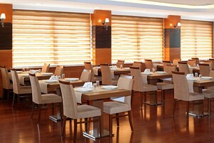 Un comedor de hotel con varias mesas y sillas, paneles de madera y lámparas fijadas a la pared.
