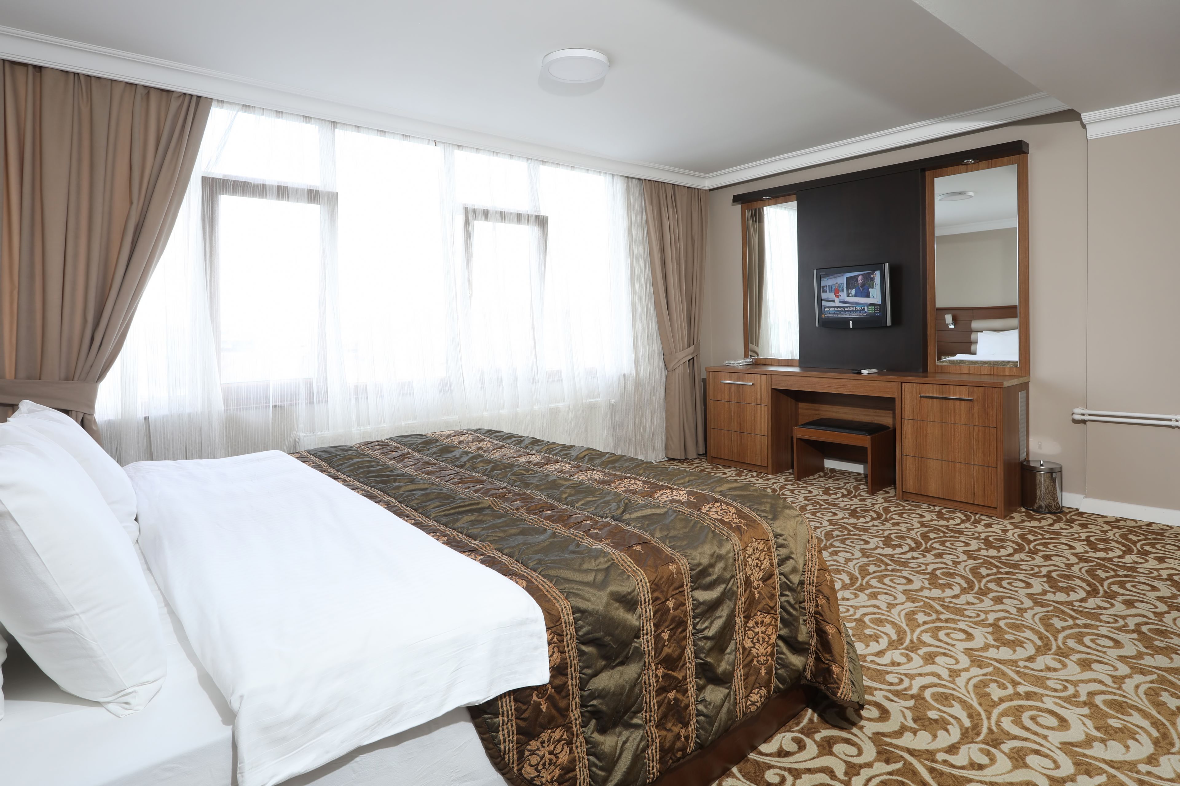 A hotel room with a large bed, a wooden dresser, a television, and a mirror.