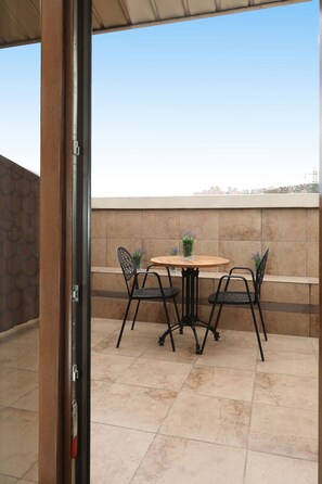 Un patio con una mesa redonda y cuatro sillas, un florero de vidrio con flores y una vista de la ciudad al fondo.