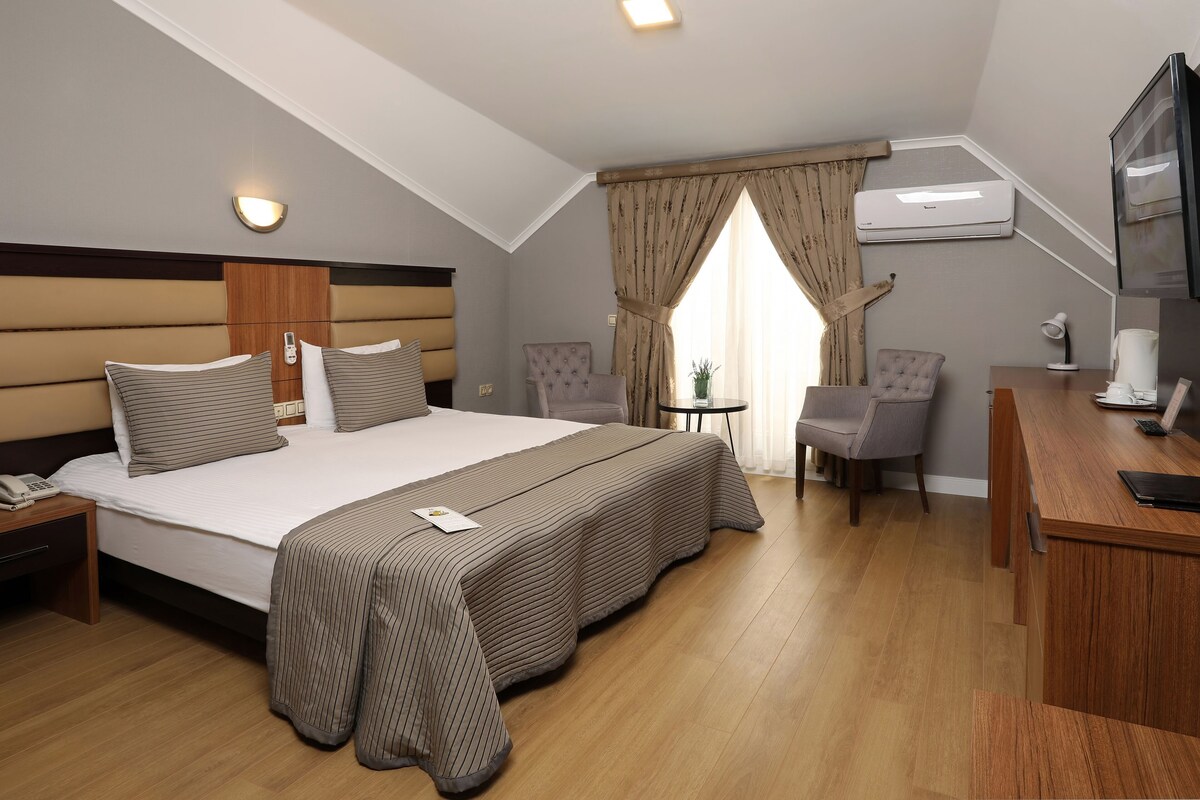 Una habitación de hotel con una cama grande, un escritorio, una silla, un aire acondicionado y un televisor.
