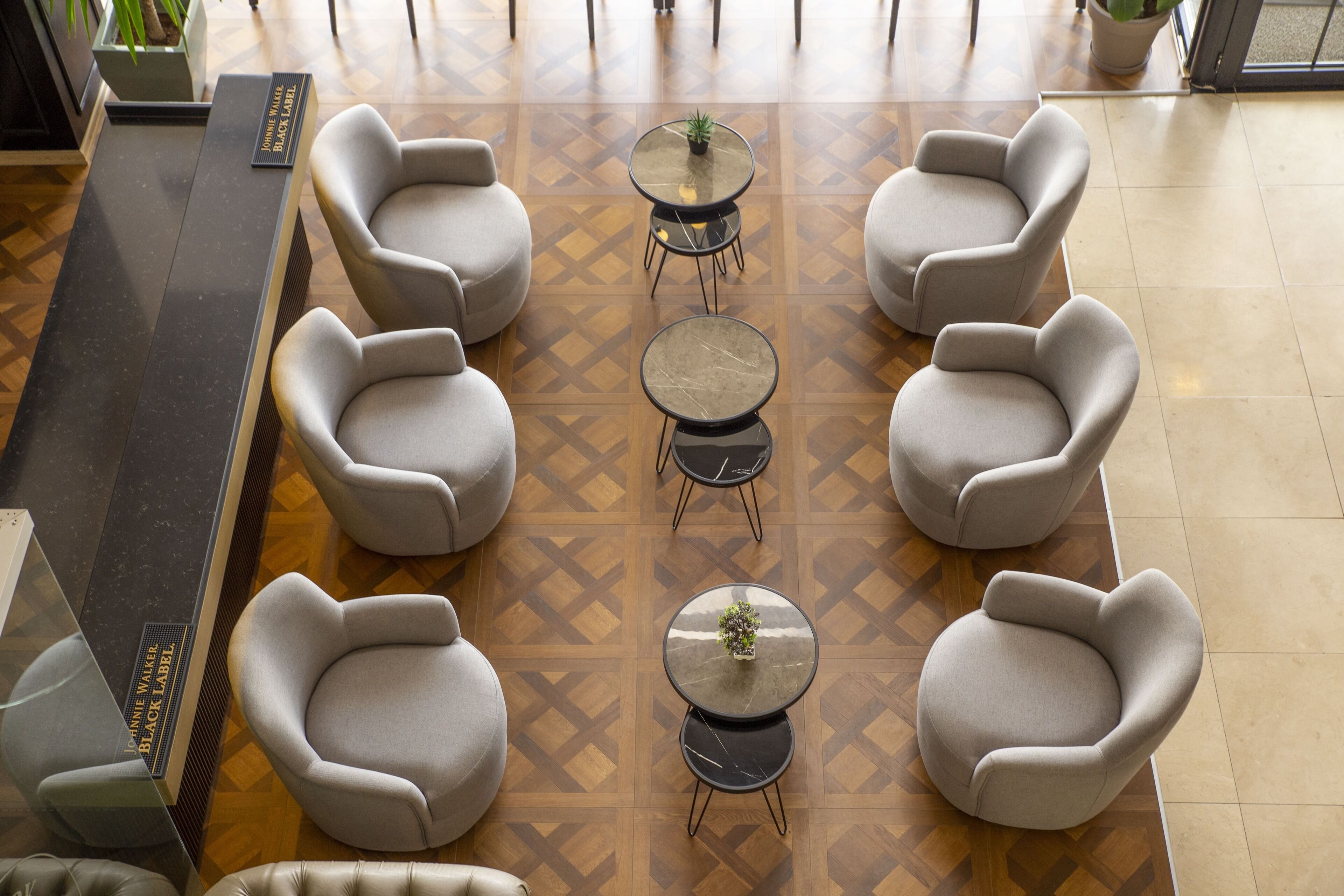 A lobby with a central seating area featuring round tables and cushioned chairs, a reception desk, and a patterned floor.