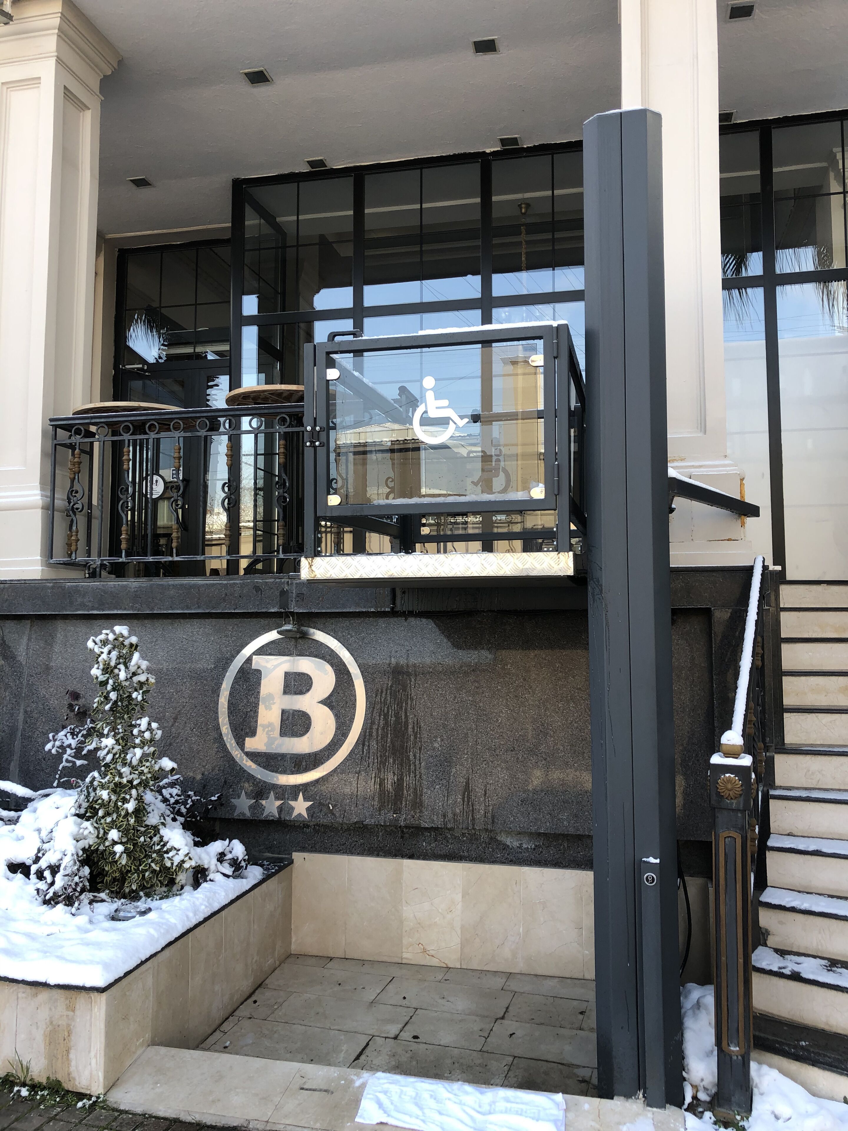A hotel entrance with a wheelchair accessibility sign, a snow-covered outdoor area, and a prominent 'B' logo on the wall.